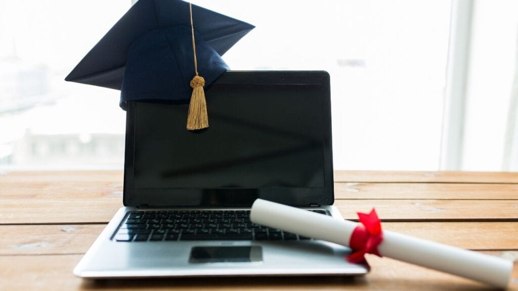 blank screen laptop with graduate cap and graduate diploma next to it