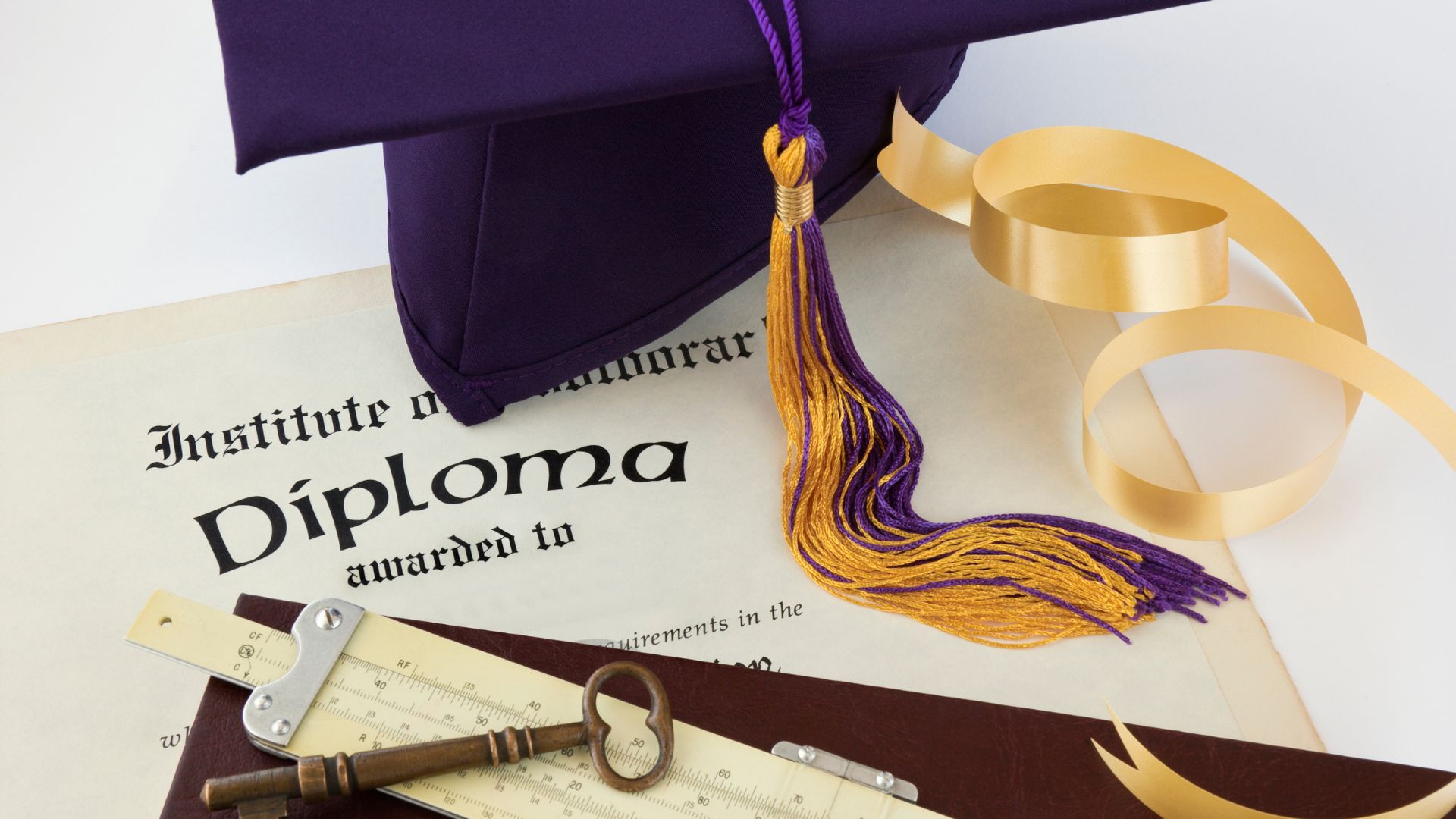 college diploma with brass skeleton key on a table next to a purple and yellow graduate cap and gold ribbon