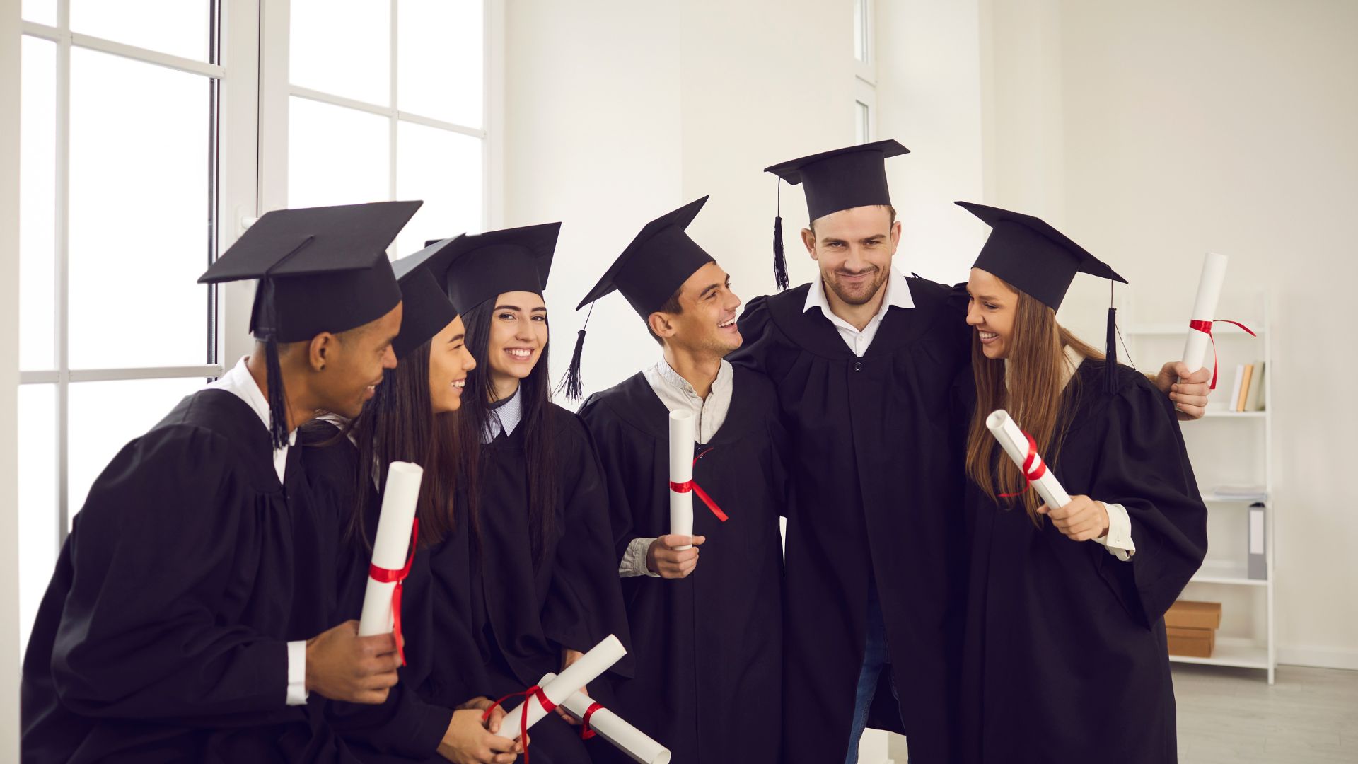 graduates standing around in cap and gowns holding uk college diplomas
