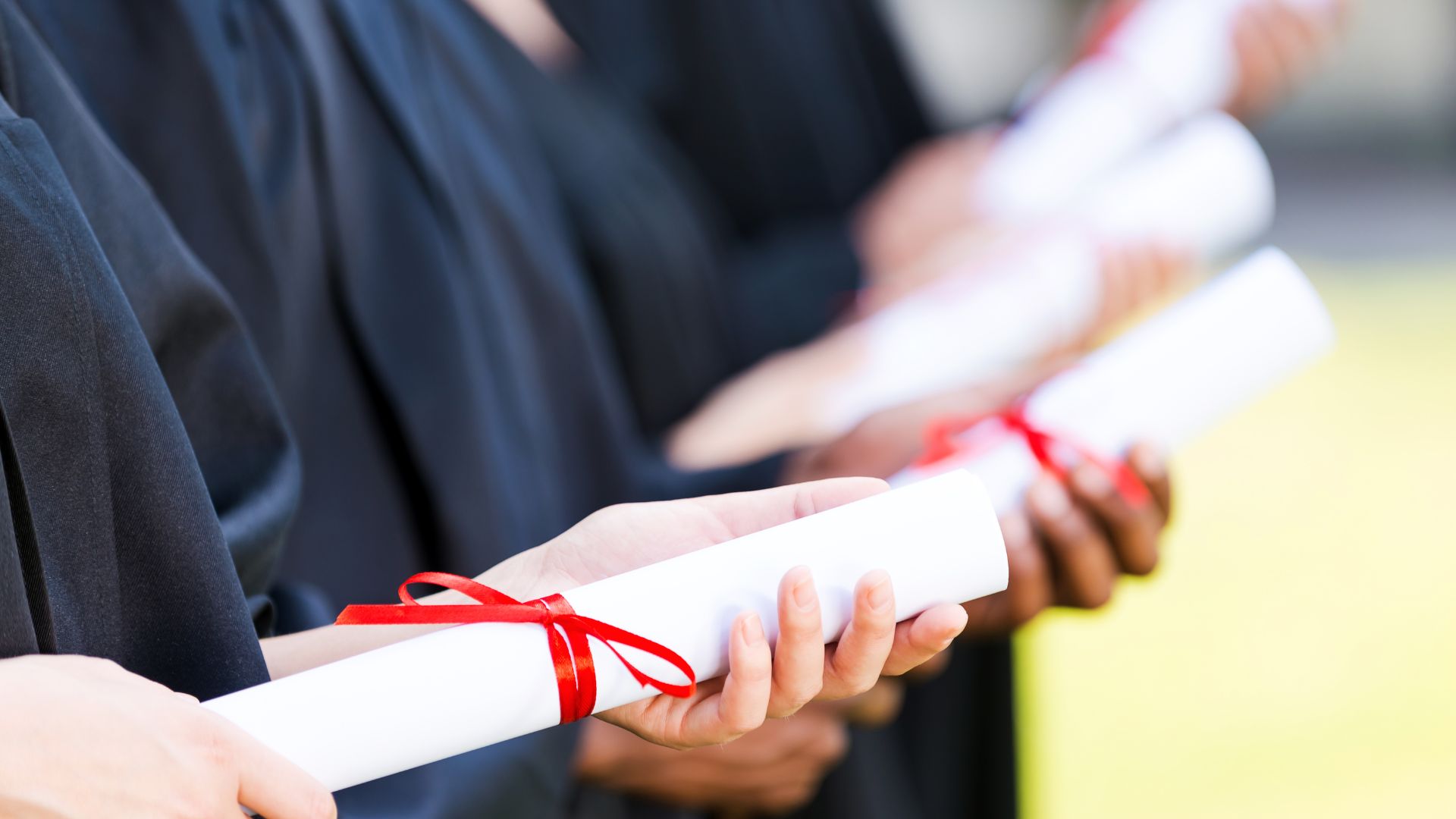graduates holding diplomas tied up in red ribbon